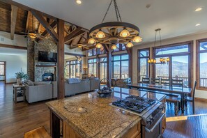 A spacious kitchen with a large island, a stone fireplace, and a stone wall. - Banner Crest - Mountain Luxury! Views, hot Tub, Private Pool and Tennis Courts, Game Room (Banner Elk)