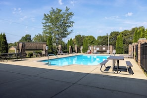 Ein Swimmingpool mit Picknicktisch und Liegestühlen, umgeben von einer Ziegelmauer und Bäumen.