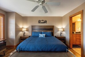 Ein Schlafzimmer mit einem Bett, zwei Nachttischen mit Lampen, einem Deckenventilator, einem Holz-Kopfteil und einer Wanddekoration.
