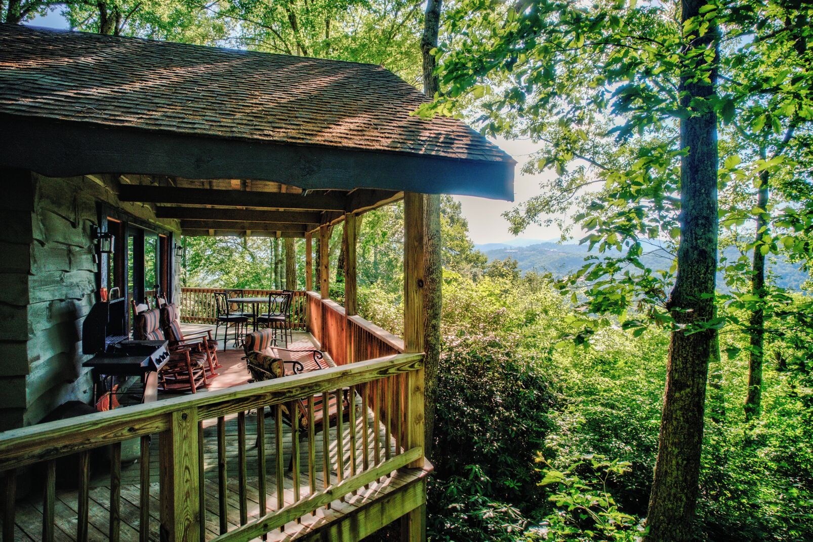 Une cabane en bois dotée d’une véranda, d’un espace salon extérieur et offrant une vue sur un paysage boisé.