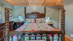 Una cama con dosel y ropa de cama floral, cabecera de madera y mesitas de noche a juego con lámparas.