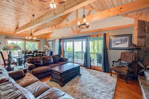 A spacious living room with a high ceiling, leather sofas, a wooden coffee table, and a large window offering a view of the outdoors. - Crystal View (Boone)