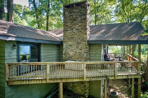 A cabin with a stone chimney, a wooden deck, and a covered outdoor seating area. - Crystal View (Boone)