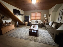 Una sala de estar acogedora con techo de madera, un sofá, una mesita de centro y un televisor.