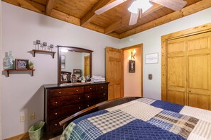 Ein Schlafzimmer mit Holzbalkendecke, einem Bett mit Patchworkdecke, einem Schminktisch, einem Spiegel und einer Tür.
