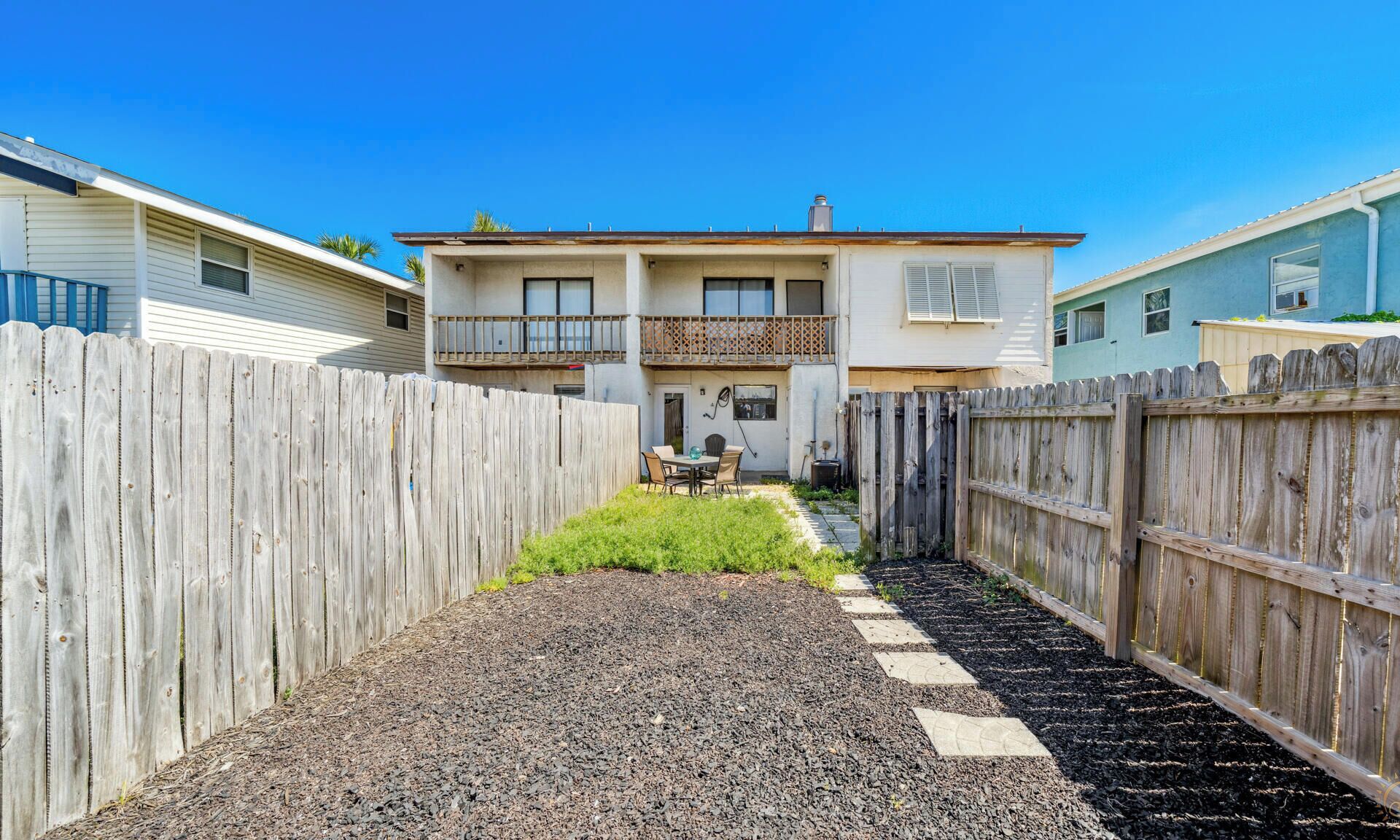 Une maison à deux étages avec un jardin clôturé, une terrasse dotée de mobilier d’extérieur et un ciel dégagé.
