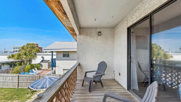 A balcony with a view of a residential area, a chair, and a wooden deck.