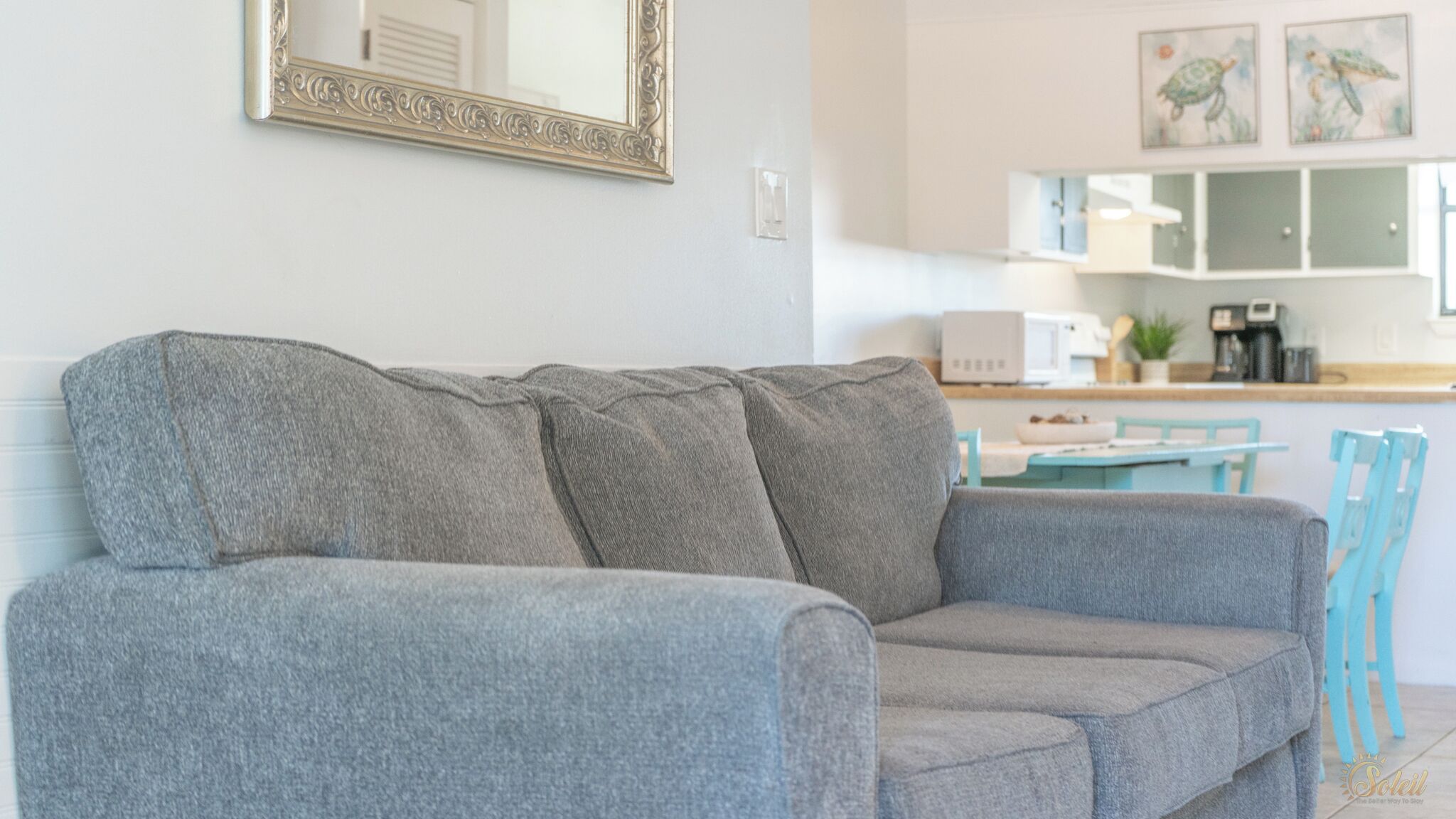 A grey sofa in a living area with a kitchen in the background.