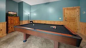 A pool table with balls, a television on a cabinet, and a wooden door. - Log Heaven (Banner Elk)