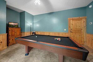 Ein Billardtisch mit Kugeln, ein Fernseher auf einem Schrank und eine Holztür.
