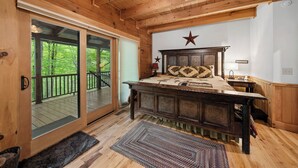 A wooden cabin bedroom with a large bed, a star decoration on the wall, and a sliding glass door leading to a deck. - Log Heaven (Banner Elk)