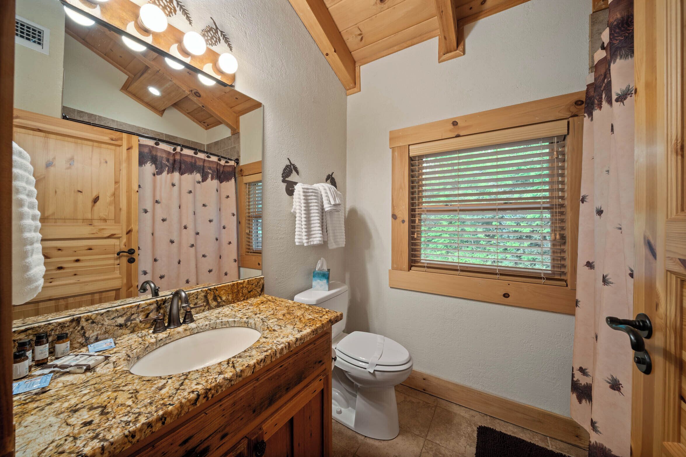 A bathroom with a wooden vanity, a sink, a toilet, and a window with blinds.