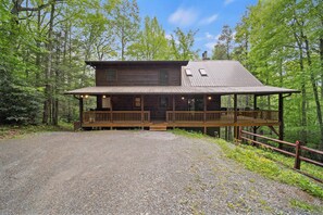Une cabane dotée d’une véranda, d’une allée en gravier et bordée par une forêt.