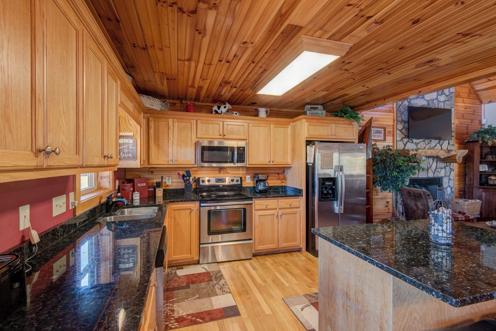 A spacious kitchen with wooden cabinets, stainless steel appliances, granite countertops, and a stone fireplace.
