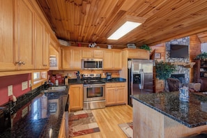 A spacious kitchen with wooden cabinets, stainless steel appliances, granite countertops, and a stone fireplace.