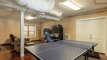 A ping pong table in a room with a brick wall, a door, and a window with blinds.