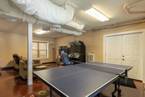 A ping pong table in a room with a brick wall, a door, and a window with blinds. - New River Ramble (Todd)