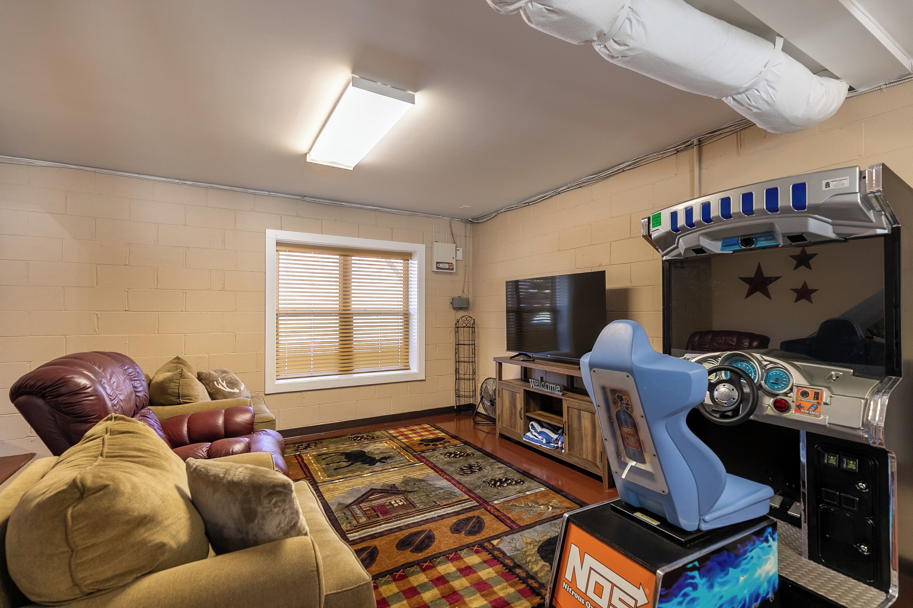Una habitación con sofá, televisión, consola de videojuegos y ventana con persianas.