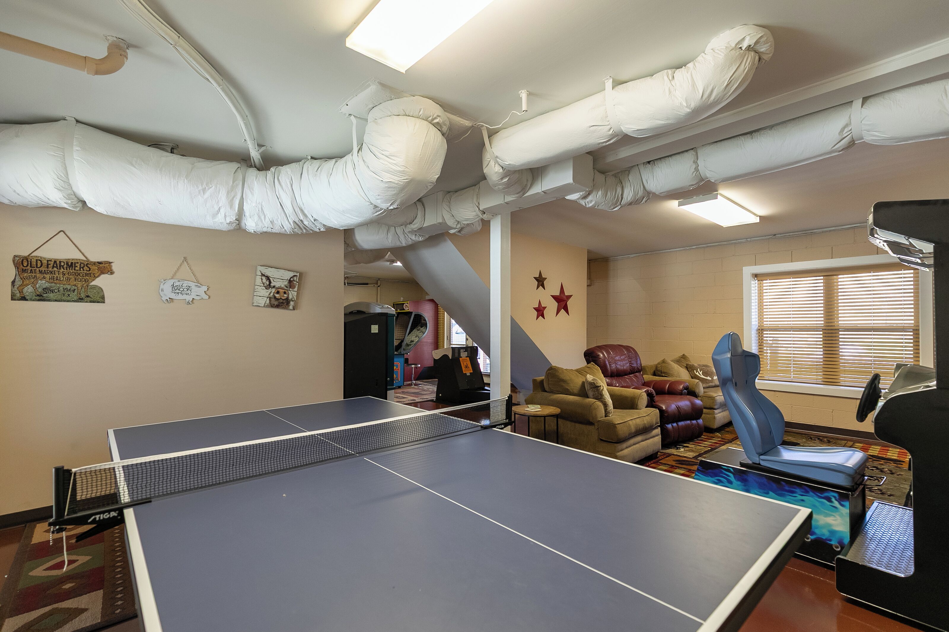 Een tafeltennistafel in een kamer met een schuine plafond, een bank en een raam met jaloezieën.