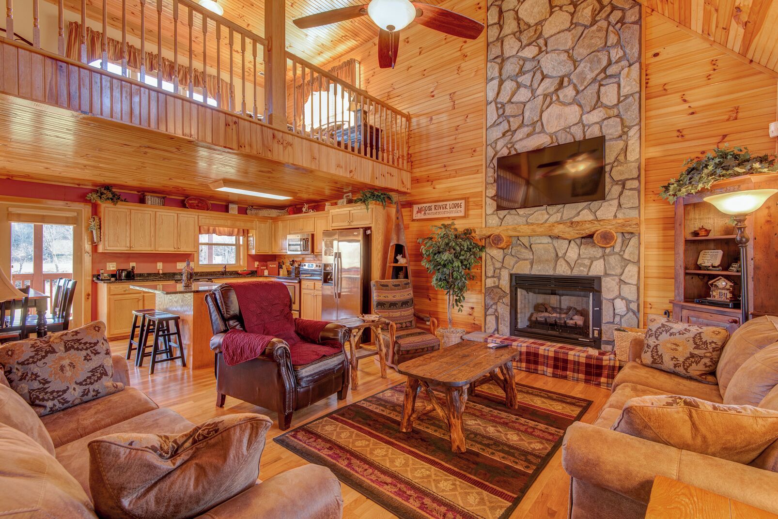 A spacious lodge interior with a stone fireplace, wooden dining area, and a cozy seating area with leather chairs.