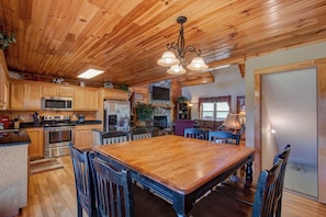 A spacious kitchen with wooden cabinets, a large dining table, and a stone fireplace. - New River Ramble (Todd)
