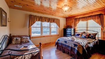 A cozy bedroom with wooden ceilings, a large bed with a patterned blanket, a smaller bed, and a dresser.