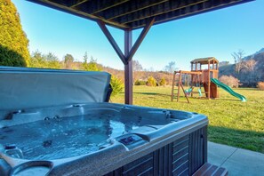 A hot tub under a wooden pergola with a playground in the background.