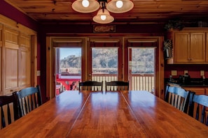 Une table à manger en bois avec des chaises, un coin cuisine avec des placards et une vue sur un paysage par la porte.