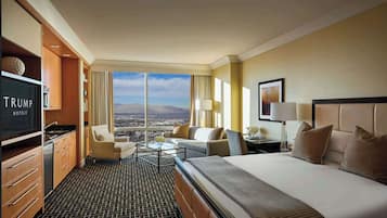 A hotel room with a bed, two armchairs, a sofa, a TV, a desk, and a large window with a city view.