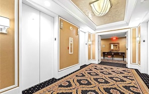Um corredor de hotel com carpete estampado, paredes brancas e um candelabro.