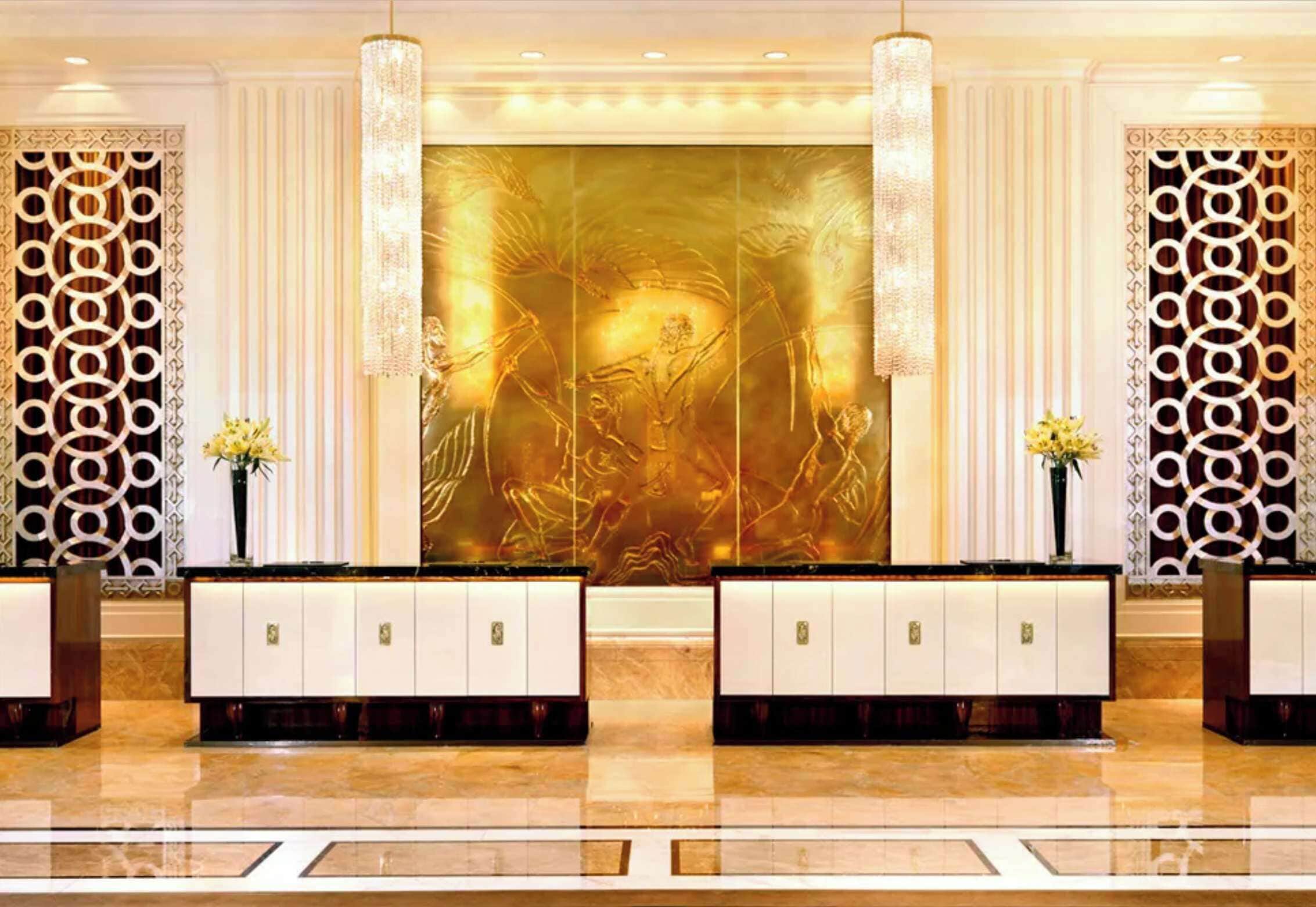 A reception area with a large golden mural, two symmetrical reception desks, and decorative wall panels.