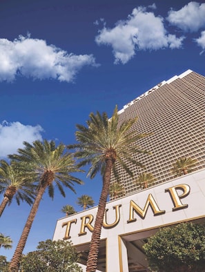 Een gebouw met de naam 'TRUMP' in grote letters op de gevel, omringd door palmbomen.