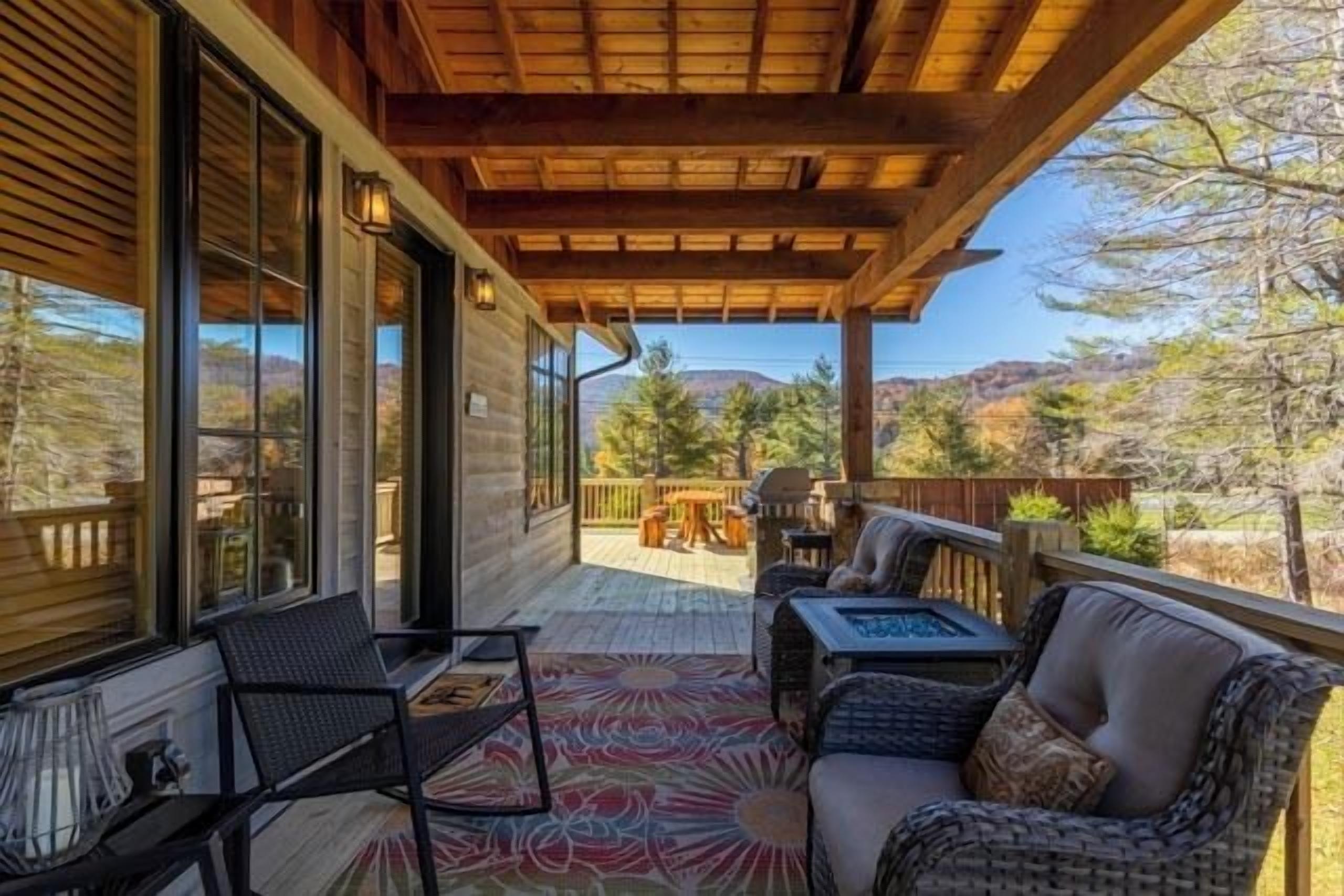 A covered patio with a view of a mountainous landscape, furnished with a sofa, chairs, and a table.