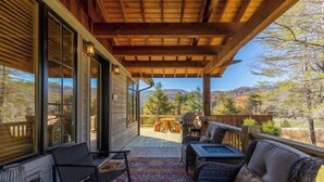 Eine überdachte Terrasse mit Blick auf eine gebirgige Landschaft, ausgestattet mit einer Couch, Stühlen und einem Tisch.