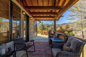 Eine überdachte Terrasse mit Blick auf eine gebirgige Landschaft, ausgestattet mit einer Couch, Stühlen und einem Tisch.