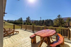 A wooden deck with a table and chairs, surrounded by a wooden railing, overlooking a mountainous landscape. - Banner Sky (Banner Elk)