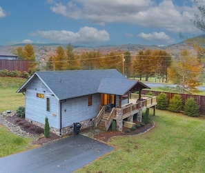 Ein Bungalow mit Veranda und kleiner Terrasse, umgeben von einem Rasen und Bäumen.