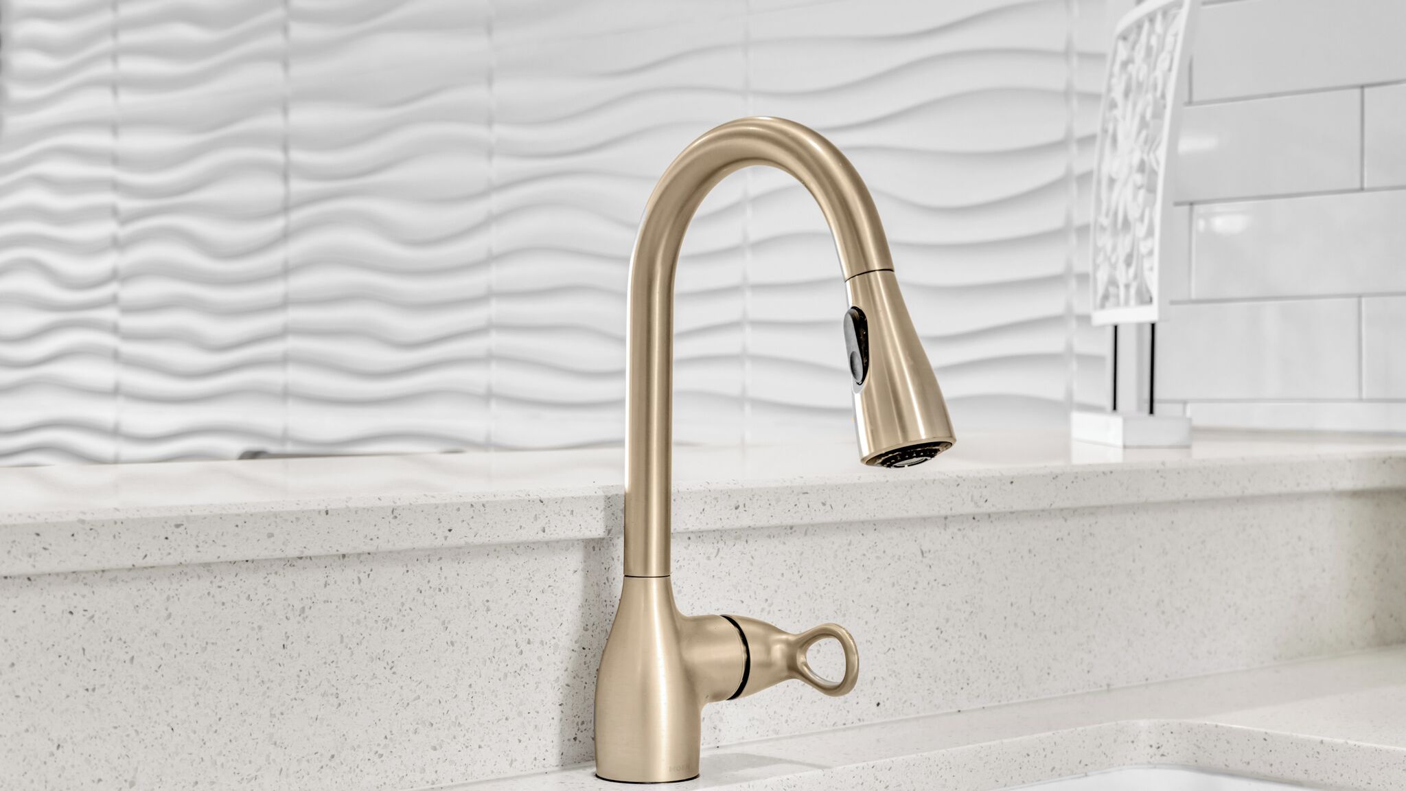A kitchen sink with a curved faucet, a backsplash with a wavy pattern, and a countertop.