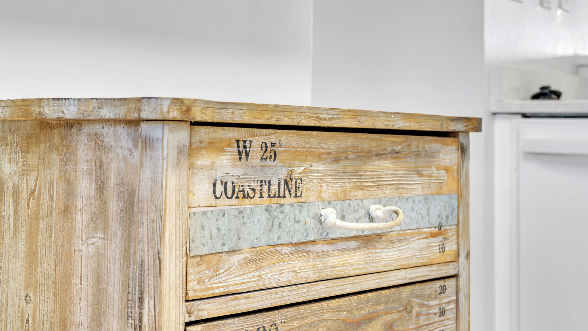 Ein Holzkabinett mit rustikaler Oberfläche, beschriftet mit 'W 25° COASTLINE' und mit einem weißen Griff.