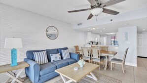 A modern living room with a sofa, coffee table, and dining area. - Commodore 210 (Panama City Beach)