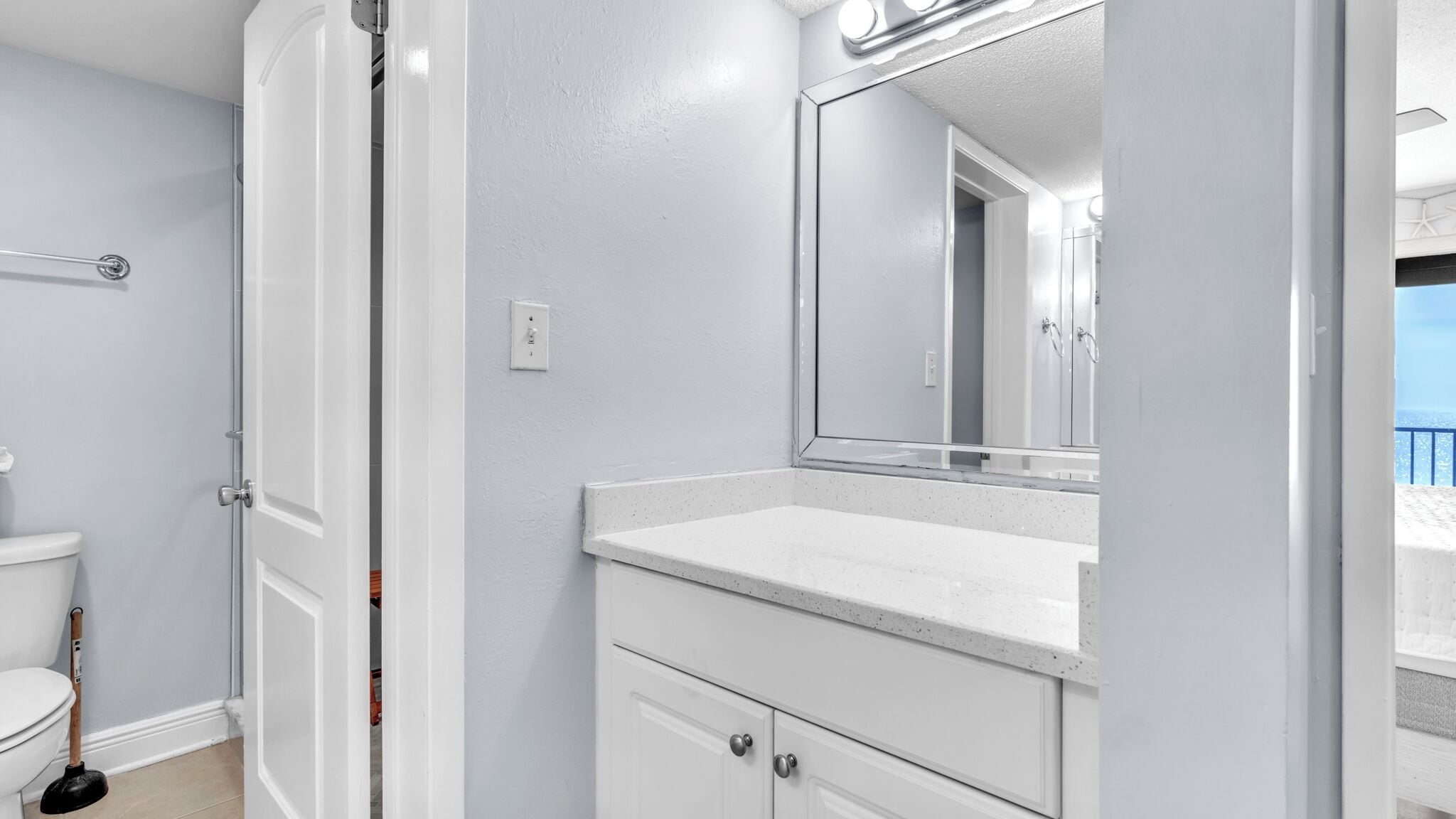 A bathroom with a toilet, a sink, a mirror, and a door leading to another room.