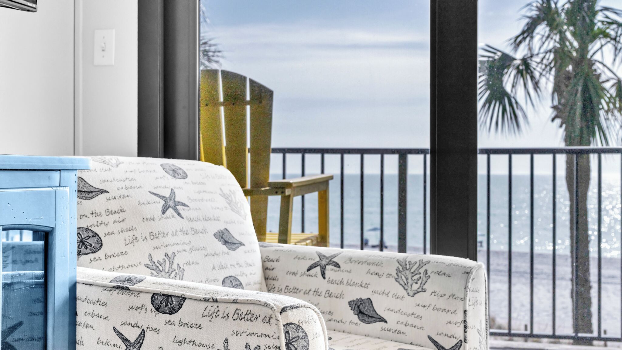 A balcony with a view of the sea, a blue cabinet, and a patterned chair.