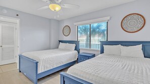 Un dormitorio con dos camas, ventilador de techo, ventana con persianas y decoración mural.