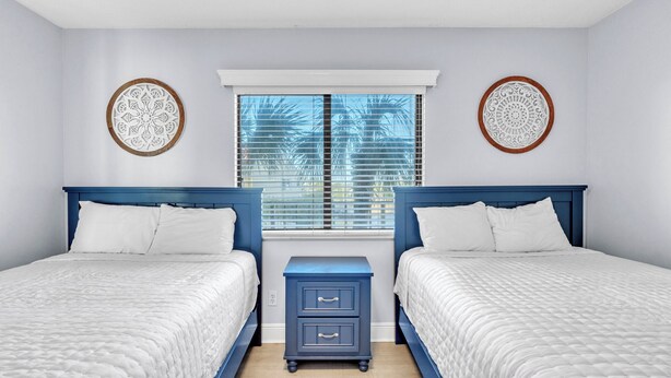 A bedroom with two beds, a window with blinds, and decorative wall art. - Commodore 210 (Panama City Beach)