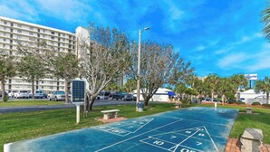 A shuffleboard court with a building in the background. - Commodore 210 (Panama City Beach)