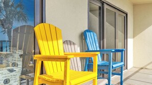 A balcony with two Adirondack chairs, one yellow and one blue, and a small table.