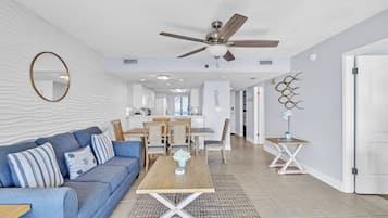 Un salon moderne avec un ventilateur de plafond, un coin repas avec une table et des chaises en bois, et une cuisine en arrière-plan.