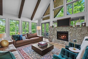 A spacious living room with a stone fireplace, large windows, and a cozy seating area. - Three Bears Retreat at Monteagle (Banner Elk)