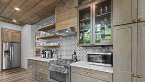 A modern kitchen with stainless steel appliances, wooden cabinets, and a built-in microwave. - Three Bears Retreat at Monteagle (Banner Elk)