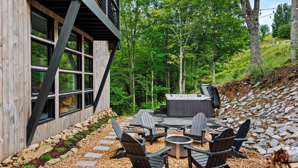 An outdoor seating area with Adirondack chairs and a fire pit, surrounded by a wooden deck and a stone pathway. - Three Bears Retreat at Monteagle (Banner Elk)